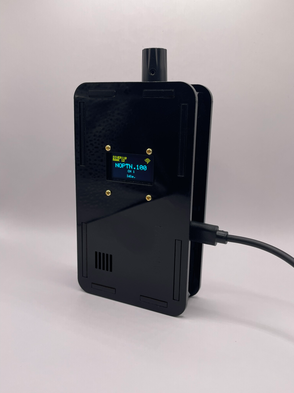 Photograph of a production TACCOM unit, screen lit, charging over USB-C